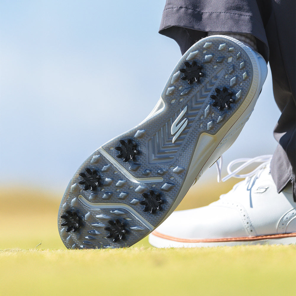 Close-up of a golf shoe with cleats on a blurred grass background