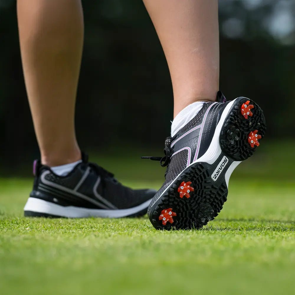 The underside of a persons golf shoe showing red and black Pivix golf spikes attached. 