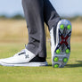 The underside of a persons golf shoe showing the green pivix golf spikes attached. 